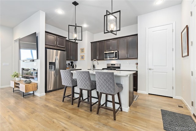 kitchen with stainless steel appliances, hanging light fixtures, dark brown cabinets, and backsplash