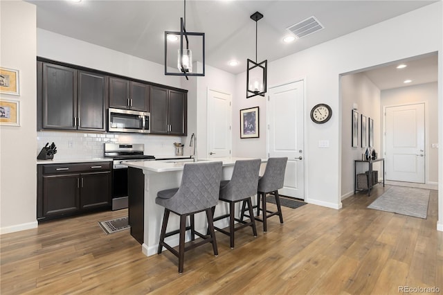 kitchen featuring pendant lighting, decorative backsplash, an island with sink, appliances with stainless steel finishes, and a breakfast bar area