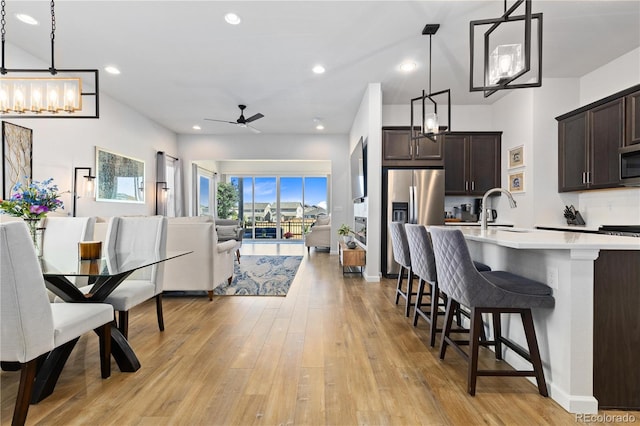 kitchen featuring dark brown cabinetry, a breakfast bar area, hanging light fixtures, appliances with stainless steel finishes, and ceiling fan with notable chandelier