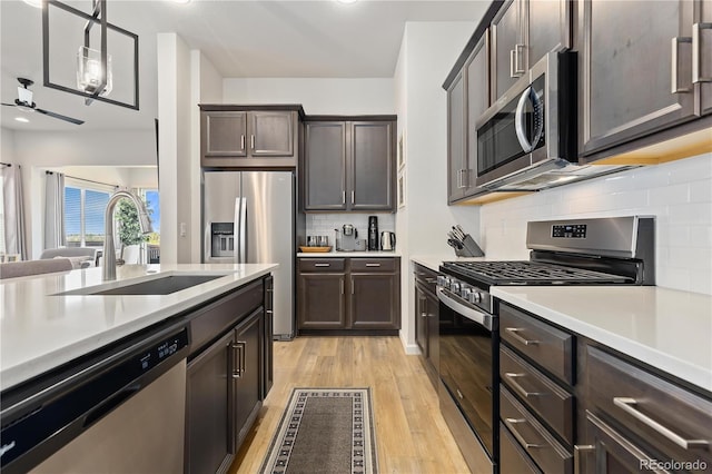 kitchen with sink, hanging light fixtures, stainless steel appliances, dark brown cabinets, and light wood-type flooring