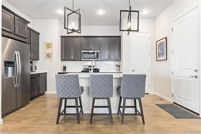 kitchen featuring dark brown cabinets, stainless steel appliances, an island with sink, a kitchen bar, and decorative light fixtures