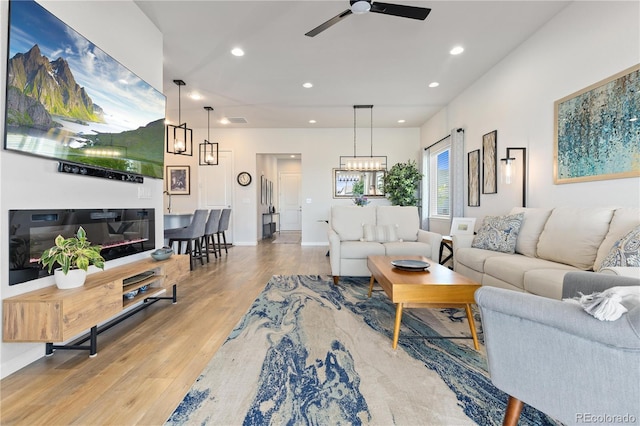 living room with ceiling fan with notable chandelier and light hardwood / wood-style flooring