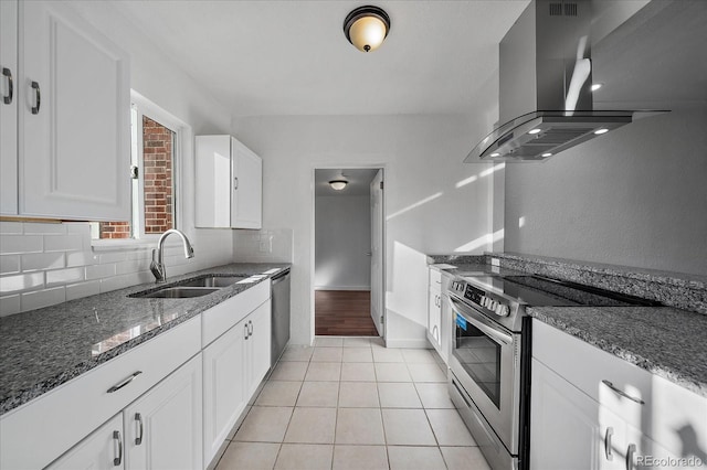 kitchen featuring appliances with stainless steel finishes, dark stone counters, wall chimney exhaust hood, sink, and white cabinetry