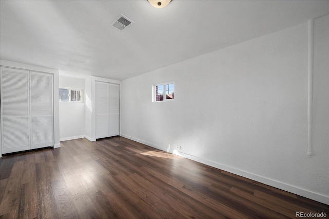 unfurnished bedroom with dark hardwood / wood-style flooring and two closets