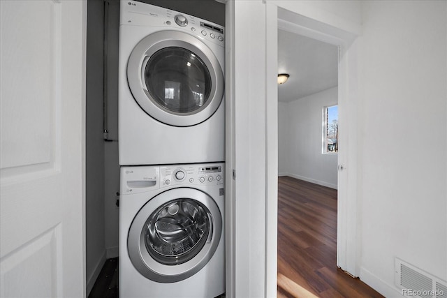 clothes washing area with stacked washer / drying machine and dark wood-type flooring