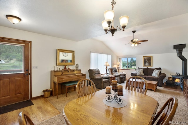 dining space with lofted ceiling, wood-type flooring, ceiling fan with notable chandelier, and a wood stove