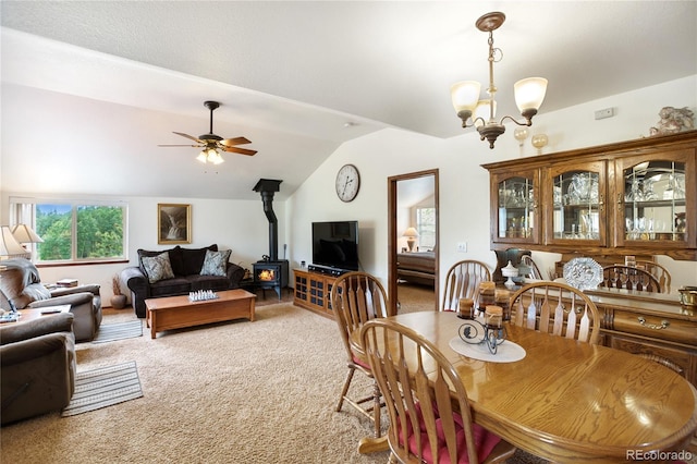 carpeted dining room featuring ceiling fan with notable chandelier, lofted ceiling, and a wood stove