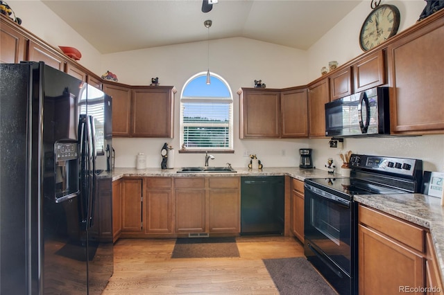 kitchen with decorative light fixtures, black appliances, sink, vaulted ceiling, and light hardwood / wood-style flooring