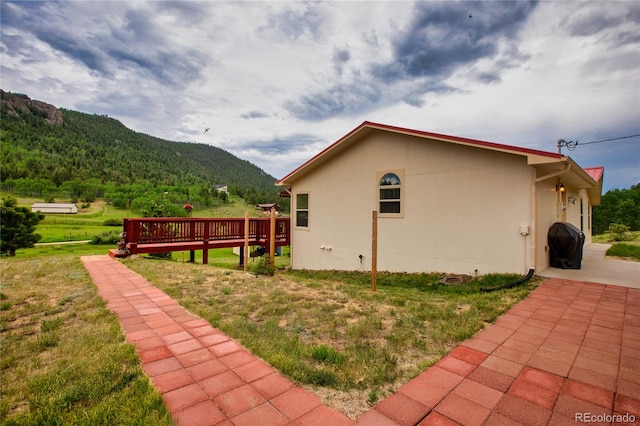 view of side of property featuring a lawn and a deck with mountain view