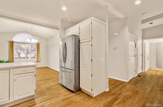 kitchen featuring light hardwood / wood-style floors, lofted ceiling, hanging light fixtures, white cabinetry, and stainless steel fridge