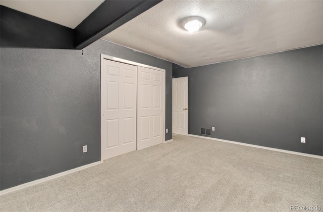 unfurnished bedroom with a closet, beamed ceiling, and light colored carpet