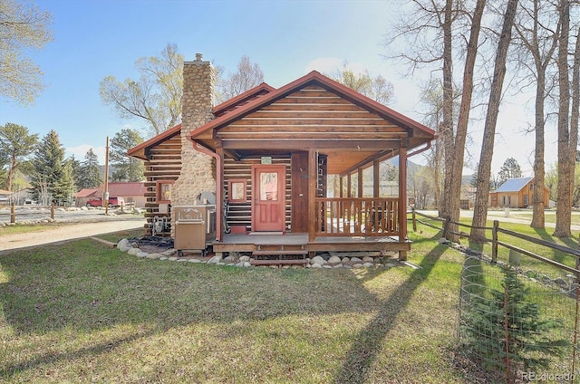 rear view of property with a lawn, fence, log siding, and a chimney