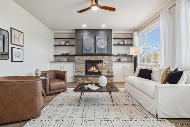 living room with light hardwood / wood-style floors, a stone fireplace, and built in features