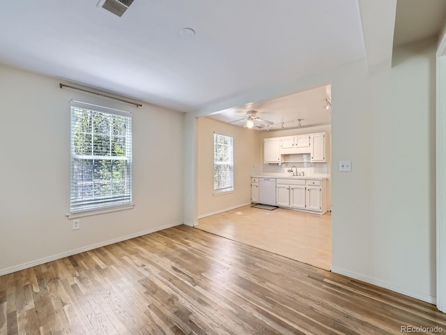 unfurnished living room with plenty of natural light, light wood-type flooring, ceiling fan, and baseboards