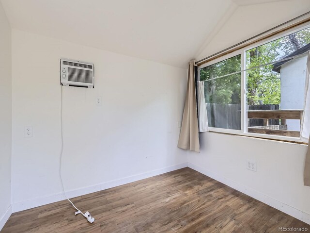 spare room featuring vaulted ceiling, wood finished floors, baseboards, and a wall mounted air conditioner