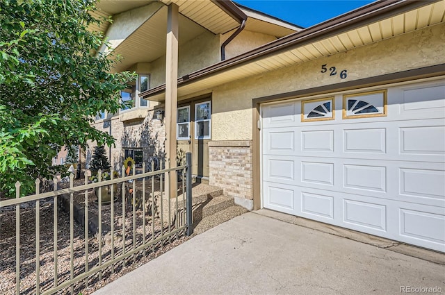 property entrance with brick siding, stucco siding, a garage, and fence