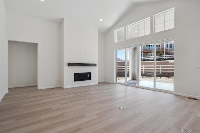 unfurnished living room with high vaulted ceiling, a glass covered fireplace, light wood finished floors, and baseboards