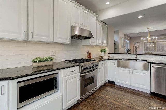 kitchen with an inviting chandelier, sink, dark stone countertops, white cabinetry, and stainless steel appliances