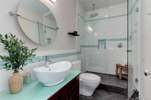 bathroom with toilet, vanity, tile walls, and tiled shower