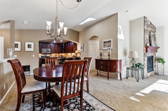 carpeted dining room featuring an inviting chandelier, a fireplace, and vaulted ceiling