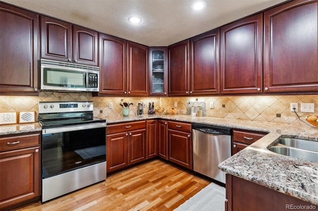 kitchen with sink, light stone counters, appliances with stainless steel finishes, light hardwood / wood-style floors, and decorative backsplash