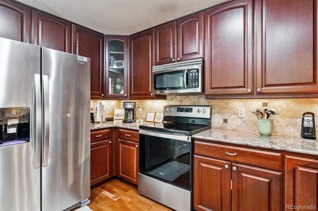 kitchen featuring light stone counters, a textured ceiling, light wood-type flooring, stainless steel appliances, and decorative backsplash