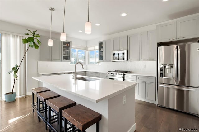 kitchen featuring sink, dark hardwood / wood-style flooring, pendant lighting, stainless steel appliances, and a kitchen island with sink