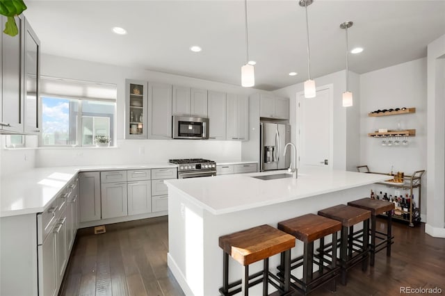 kitchen featuring pendant lighting, sink, appliances with stainless steel finishes, a kitchen island with sink, and a kitchen bar