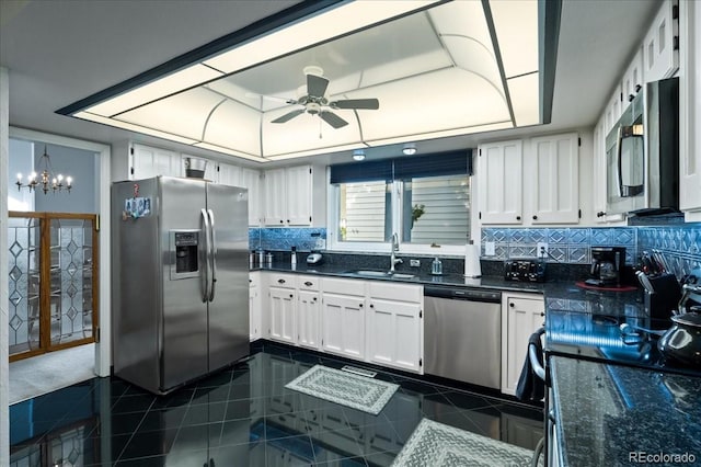 kitchen with appliances with stainless steel finishes, backsplash, a tray ceiling, sink, and white cabinetry