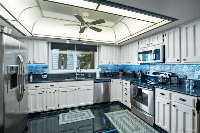 kitchen with white cabinetry, stainless steel appliances, sink, dark stone counters, and decorative backsplash