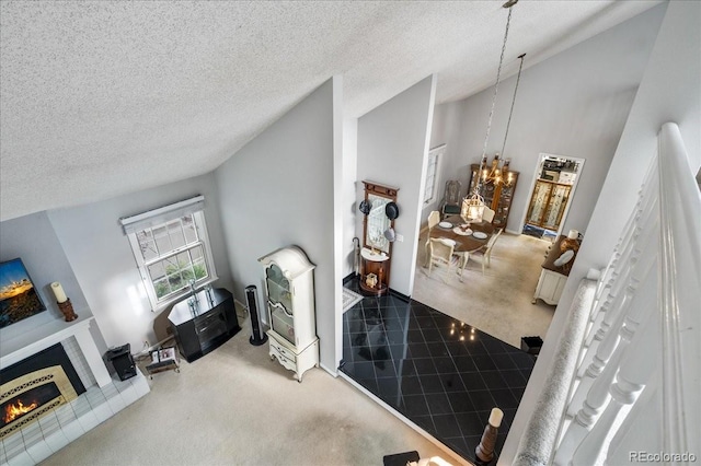 carpeted living room with a fireplace, lofted ceiling, a textured ceiling, and an inviting chandelier