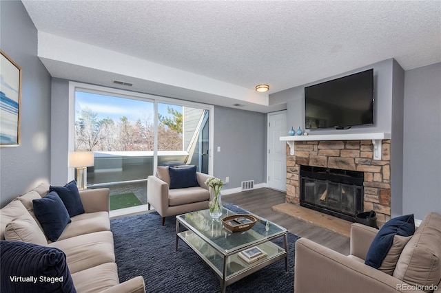 living room featuring visible vents, dark wood finished floors, a textured ceiling, and a stone fireplace