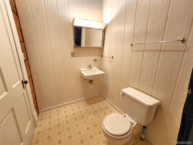 bathroom featuring sink, toilet, tile patterned floors, and wooden walls