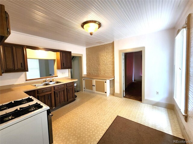 kitchen featuring light tile patterned flooring, dark brown cabinetry, white gas stove, and sink