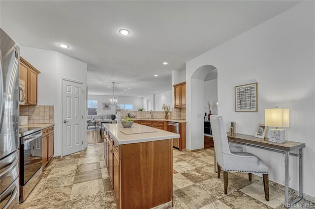 kitchen featuring kitchen peninsula, decorative backsplash, a kitchen island, and appliances with stainless steel finishes