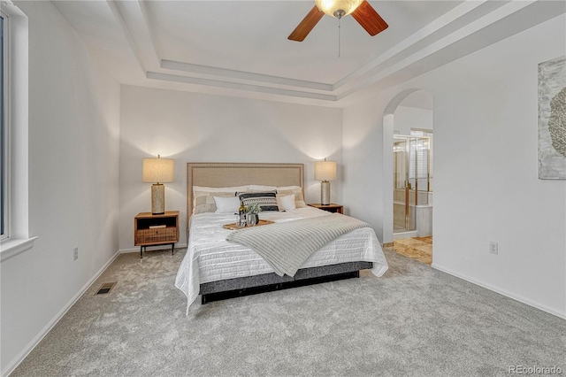 carpeted bedroom featuring ceiling fan, a raised ceiling, and ensuite bath