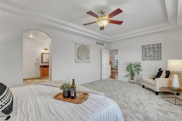 bedroom featuring carpet floors, a raised ceiling, ensuite bath, and ceiling fan