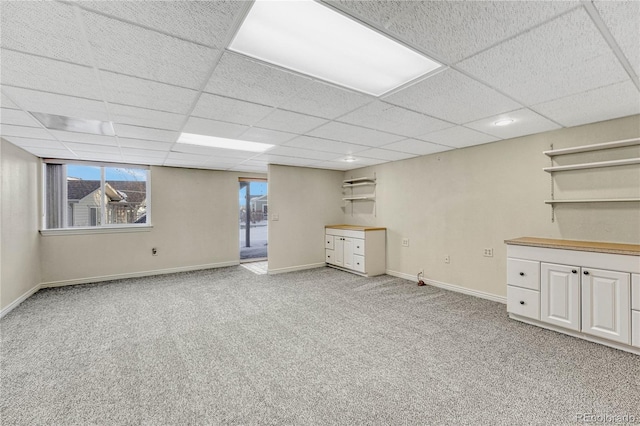 basement featuring a paneled ceiling and light colored carpet