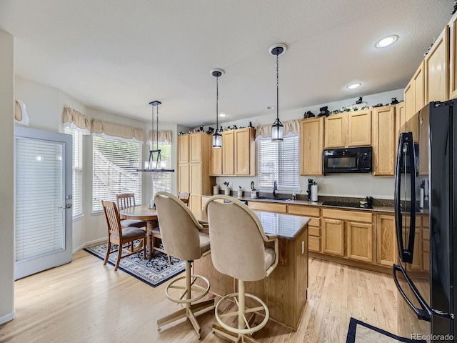 kitchen with sink, decorative light fixtures, a center island, light hardwood / wood-style flooring, and black appliances