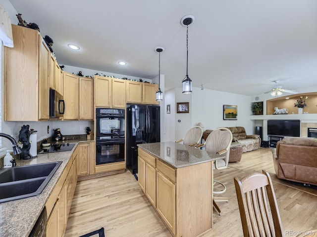 kitchen featuring a kitchen island, a breakfast bar, sink, hanging light fixtures, and black appliances