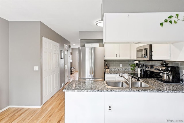 kitchen with stainless steel appliances, a peninsula, a sink, light wood finished floors, and white cabinetry