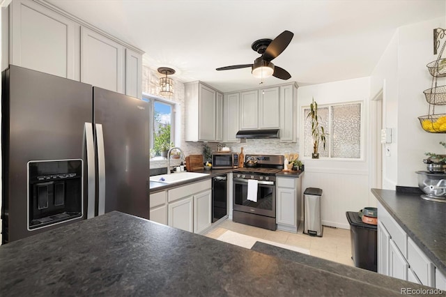 1760 W 74th Way, Denver, CO 80221 - kitchen featuring appliances with stainless steel finishes, dark countertops, light tile patterned floors, a ceiling fan, and under cabinet range hood