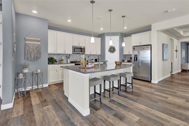 kitchen with dark wood-style flooring, dark countertops, appliances with stainless steel finishes, white cabinets, and an island with sink