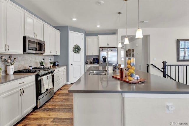 kitchen with decorative backsplash, wood finished floors, a center island with sink, white cabinets, and appliances with stainless steel finishes