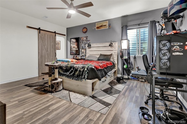 bedroom featuring baseboards, ceiling fan, a barn door, and wood finished floors
