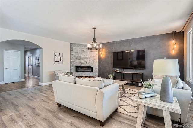 living area featuring arched walkways, a large fireplace, baseboards, and wood finished floors