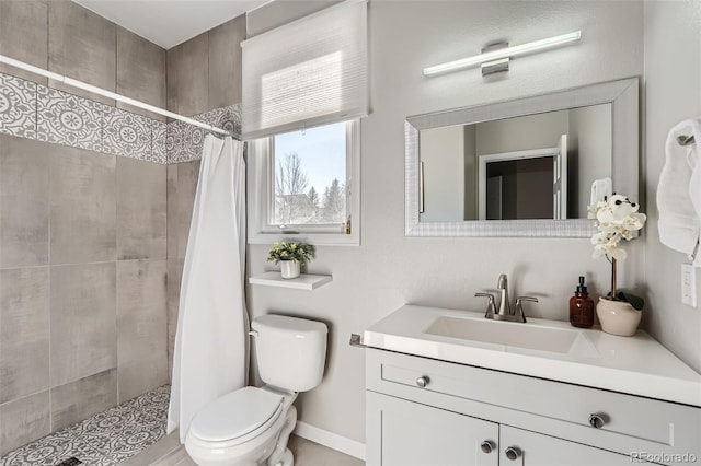 bathroom with toilet, baseboards, tiled shower, and vanity