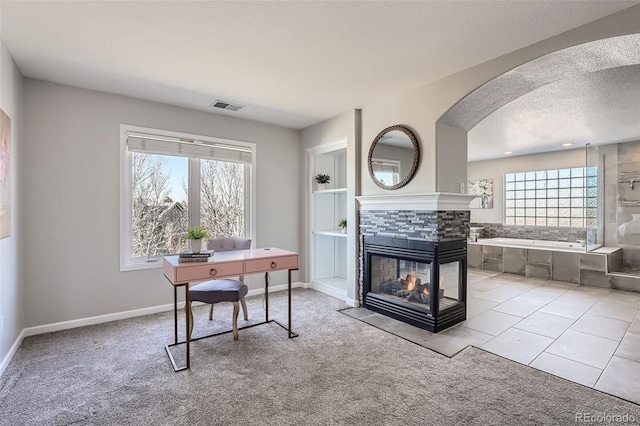 office with a textured ceiling, a wealth of natural light, a multi sided fireplace, and visible vents