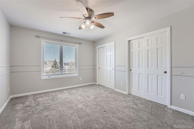 unfurnished bedroom featuring baseboards, visible vents, ceiling fan, carpet flooring, and multiple closets