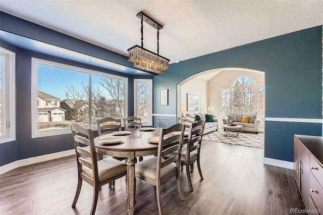 dining area featuring baseboards, arched walkways, dark wood finished floors, and a textured ceiling